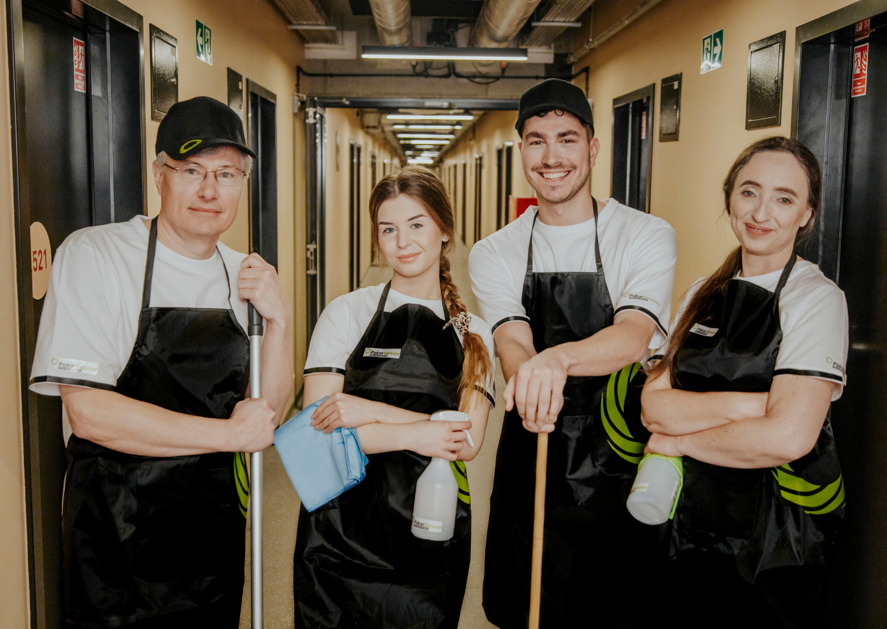 Zespół pracowników firmy sprzątającej Pakar Service w uniformach, stojących z profesjonalnym sprzętem do utrzymania czystości w korytarzu centrum handlowego.