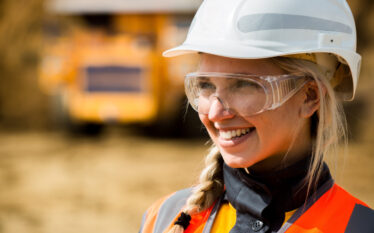 Uśmiechnięta kobieta inżynier w kasku i okularach ochronnych na terenie kopalni