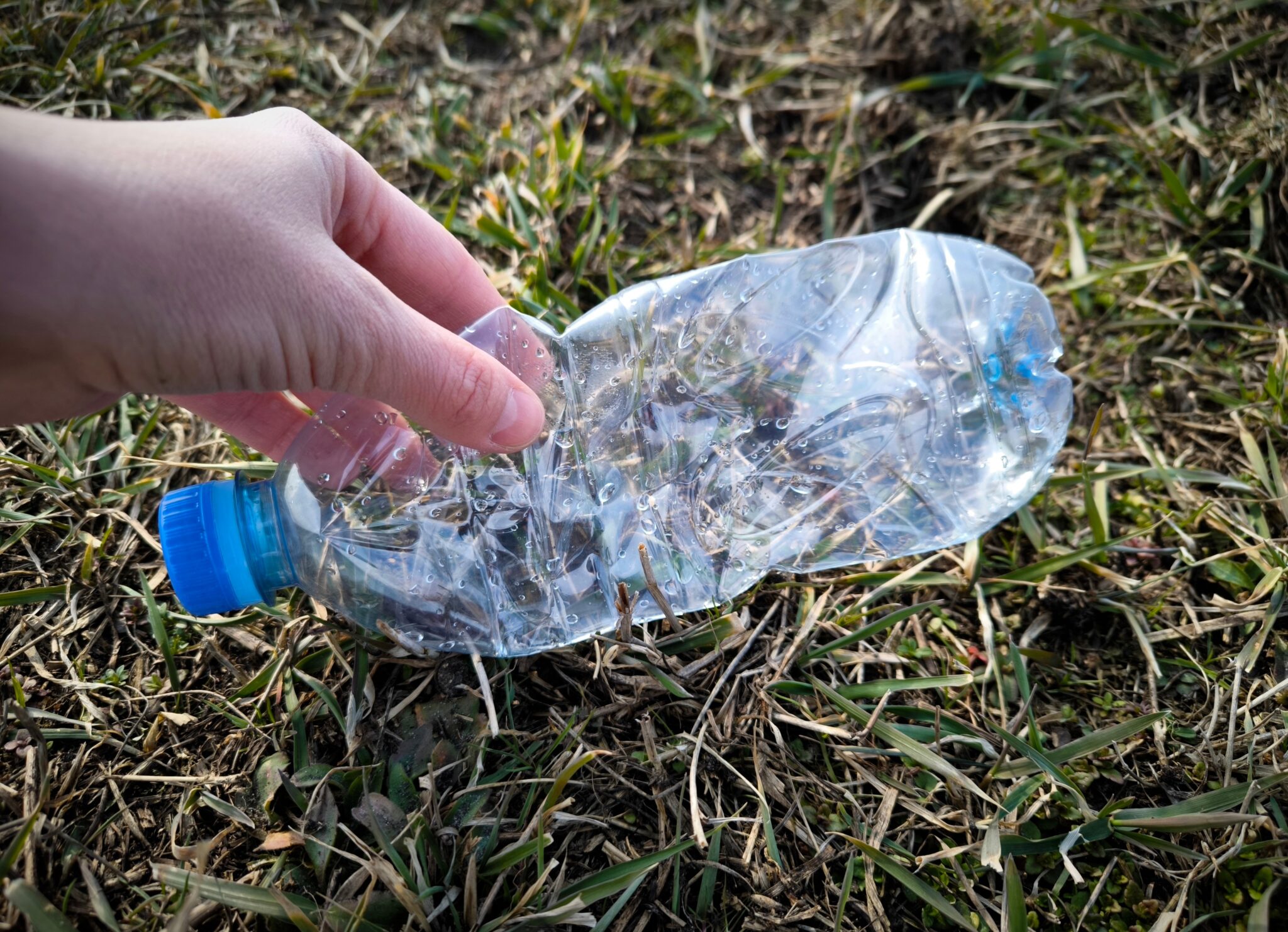 Dłoń podnosząca zgniecioną plastikową butelkę z trawy