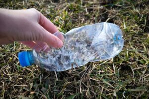 Dłoń podnosząca zgniecioną plastikową butelkę z trawy