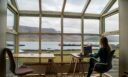 Kobieta pracująca na laptopie w biurze z panoramicznym widokiem na port i góry
