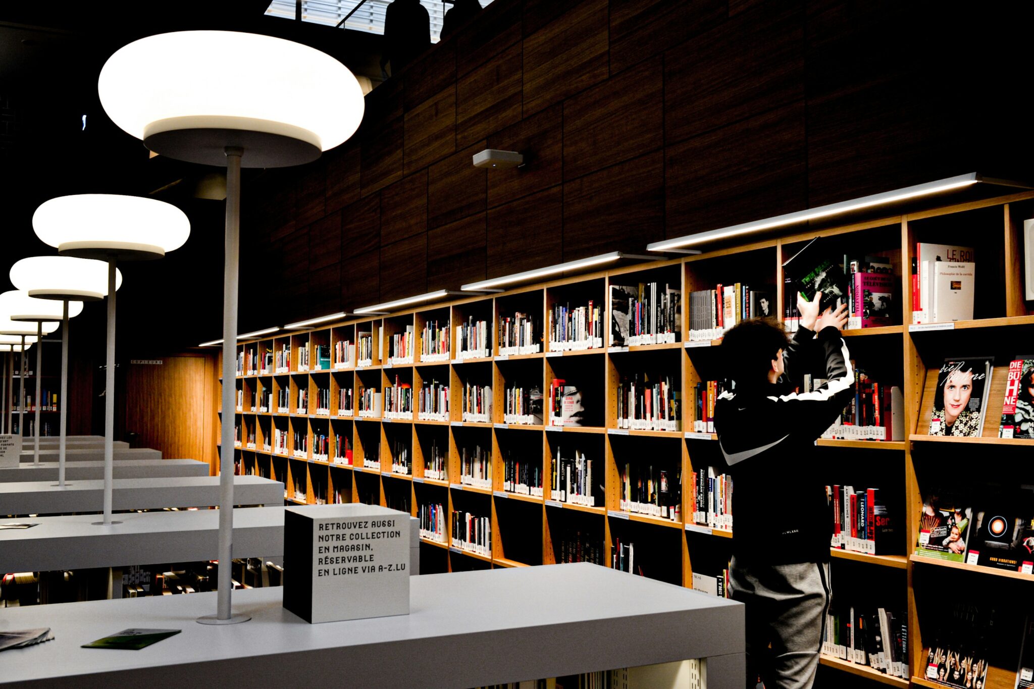 Osoba sięgająca po książkę w nowoczesnej bibliotece, symbolizująca rozwój wiedzy i edukację