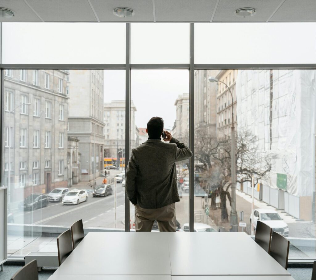 Mężczyzna rozmawiający przez telefon przy oknie w biurze z widokiem na miasto