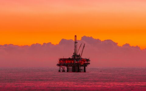 Platforma wiertnicza na morzu w blasku zachodzącego słońca symbolizująca przemysł paliwowy i emisje CO₂