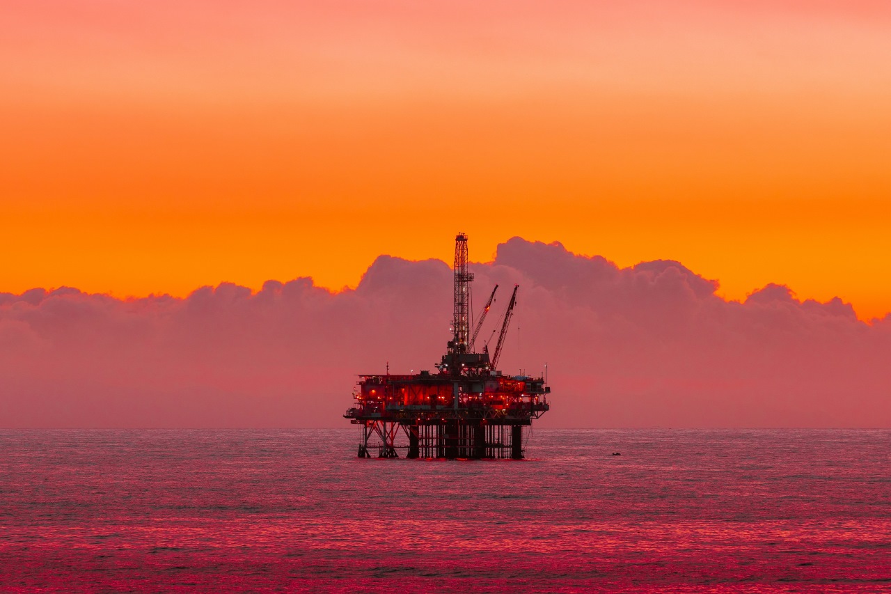 Platforma wiertnicza na morzu w blasku zachodzącego słońca symbolizująca przemysł paliwowy i emisje CO₂