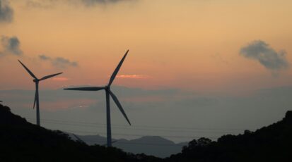Turbiny wiatrowe na tle zachodzącego słońca symbolizujące transformację energetyczną.