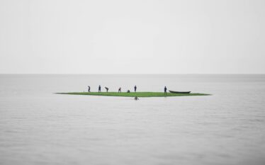 Ludzie stojący na małej wyspie pośród wody symbolizujący kruchość i wspólne wyzwania wobec zmian klimatycznych