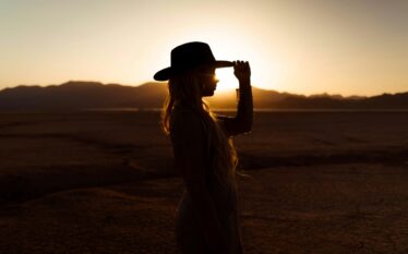 Sylwetka kobiety w kapeluszu na pustynnym tle o zachodzie słońca.