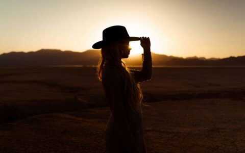 Sylwetka kobiety w kapeluszu na pustynnym tle o zachodzie słońca.