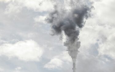 Kominy przemysłowe emitujące ciemny dym na tle pochmurnego nieba