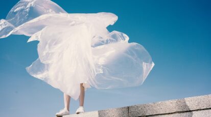 Osoba stojąca na murze z unoszącą się na wietrze przezroczystą folią plastikową na tle błękitnego nieba