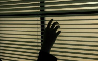 Dłoń odsuwająca żaluzje w ciemnym pomieszczeniu