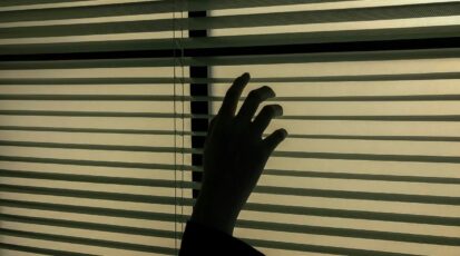 Dłoń odsuwająca żaluzje w ciemnym pomieszczeniu