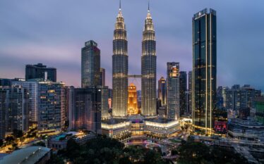 Panorama Kuala Lumpur nocą z oświetlonymi wieżami Petronas Towers i nowoczesną zabudową centrum miasta.