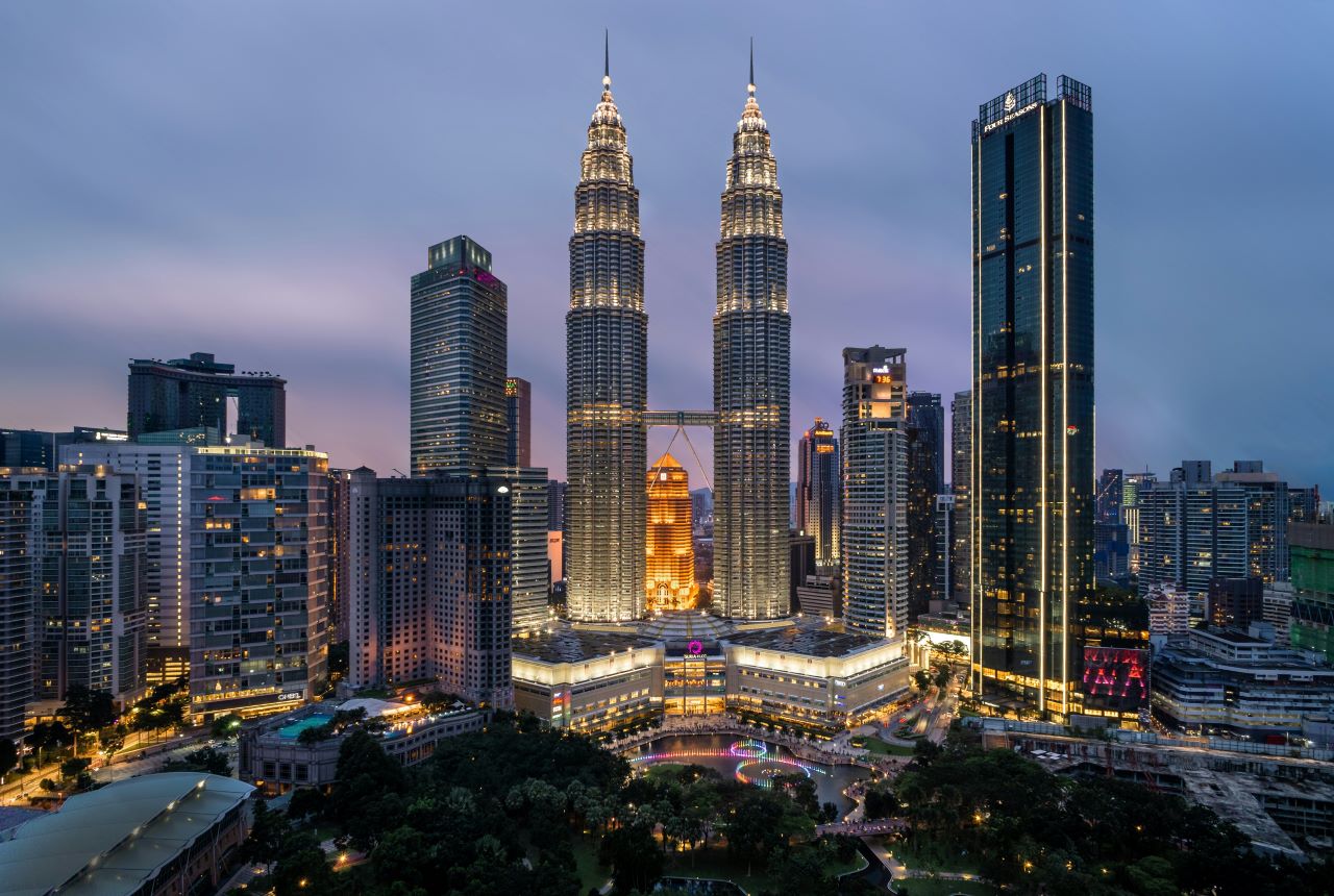 Panorama Kuala Lumpur nocą z oświetlonymi wieżami Petronas Towers i nowoczesną zabudową centrum miasta.