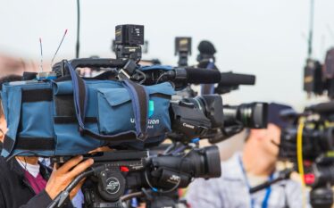 Kamery telewizyjne ustawione w rzędzie podczas wydarzenia medialnego, symbolizujące rolę mediów w relacjonowaniu tematów publicznych
