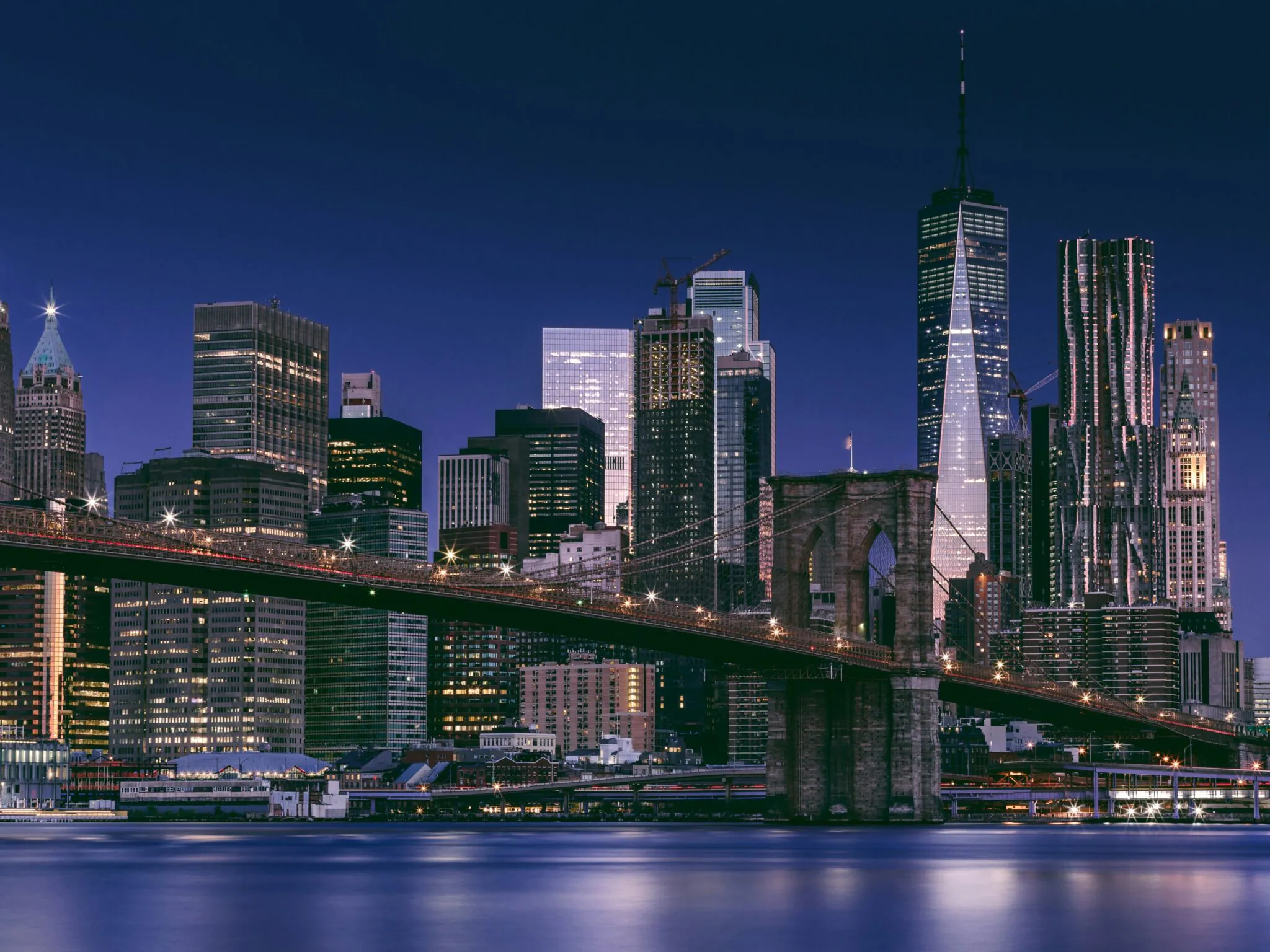 Panorama nowojorskiego Manhattanu nocą z mostem Brooklińskim na pierwszym planie