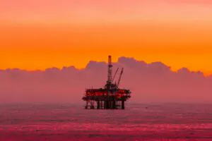 Platforma wiertnicza na morzu w blasku zachodzącego słońca symbolizująca przemysł paliwowy i emisje CO₂