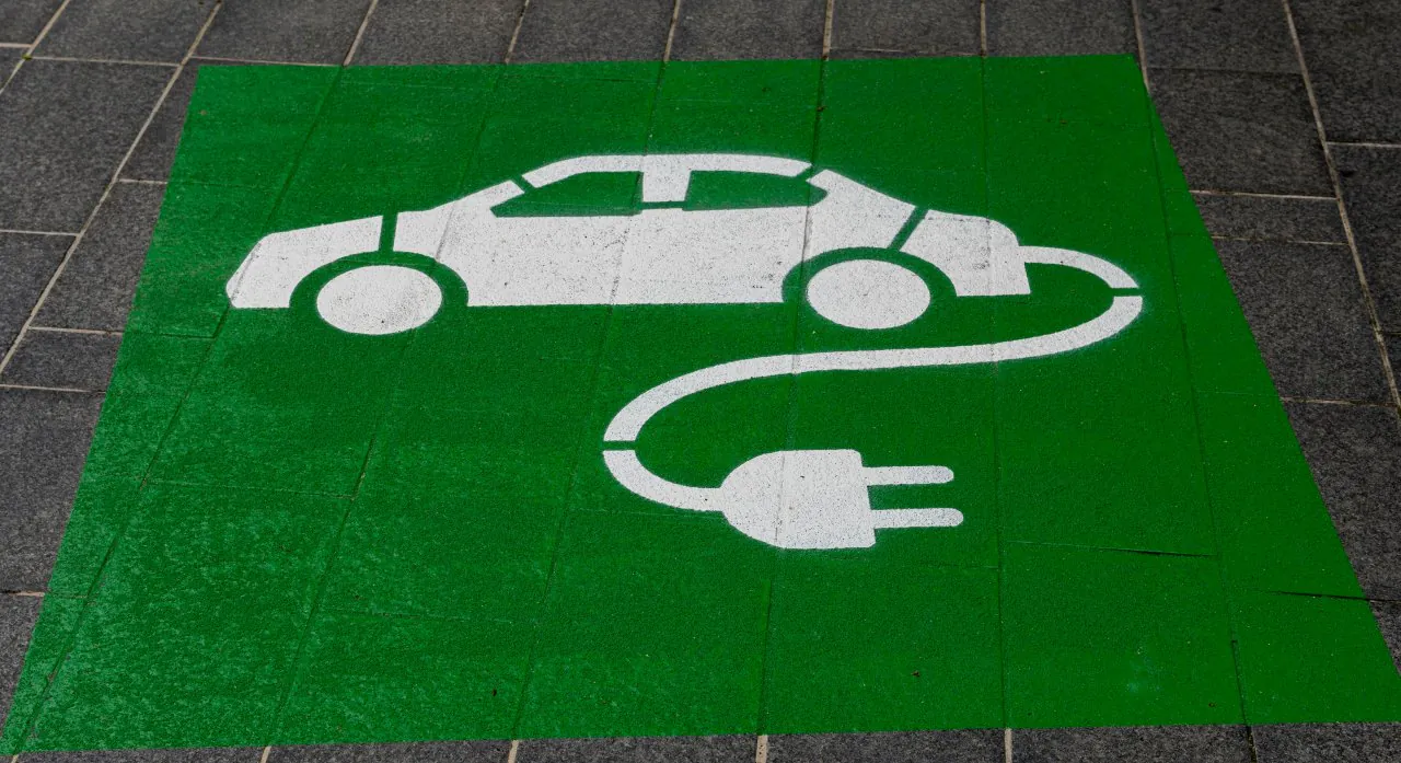 Symbol samochodu elektrycznego z wtyczką namalowany na zielonym tle oznaczającym strefę ładowania