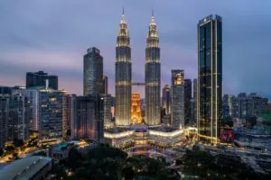 Panorama Kuala Lumpur nocą z oświetlonymi wieżami Petronas Towers i nowoczesną zabudową centrum miasta.