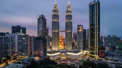Panorama Kuala Lumpur nocą z oświetlonymi wieżami Petronas Towers i nowoczesną zabudową centrum miasta.